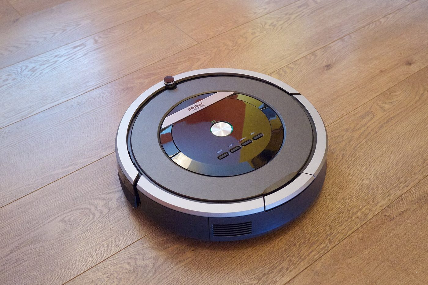 A Roomba robotic vacuum cleaner working across a wooden floor.